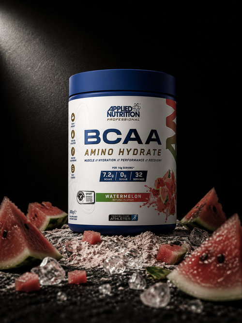 Applied Nutrition BCAA Amino Hydrate Watermelon supplement tub on dark volcanic stone with scattered watermelon pieces, amino crystals and hydration powder.